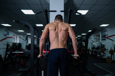 Shirtless man doing triceps dips from parallel bars in gym