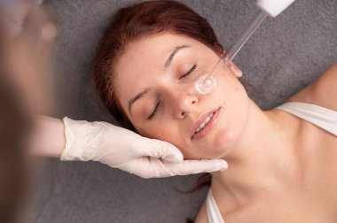 Doktor, kadın bir hastanın yüzündeki sivilce için darsonval aparatı kullanıyor.