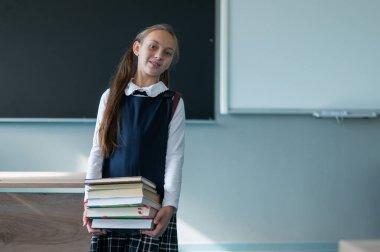Sırt çantalı beyaz bir kızın portresi. Kız sınıfta bir yığın ders kitabı tutuyor.