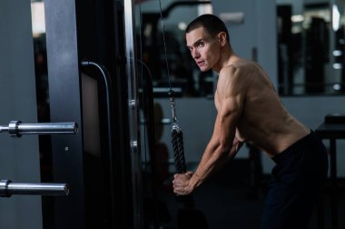 Shirtless man doing triceps pulldown at the gym