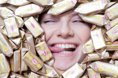 The face of a Caucasian woman surrounded by Rakhat chocolates. The girl shows her tongue.