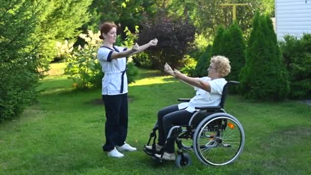 Bir Hemşire Dışarıda Tekerlekli Sandalyede Yaşlı Bir Hastayla Egzersiz Yapıyor — Stok video