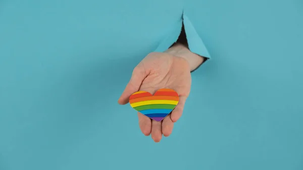 Hand Rainbow Colored Heart Sticking Out Hole Blue Cardboard Background — Fotografia de Stock