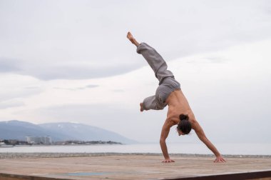 Üstsüz beyaz adam sahilde akrobatik tekerlek yapıyor.