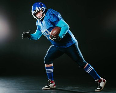 Amerikan futbolu için mavi üniformalı bir adamın portresi siyah arka planda bir topla koşuyor.