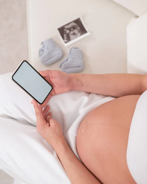 Těhotná Žena Bez Tváře Sedí Bílé Pohovce Drží Smartphone Fetální — Stock fotografie