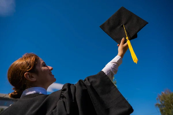 A woman throws her graduation cap against the blue sky