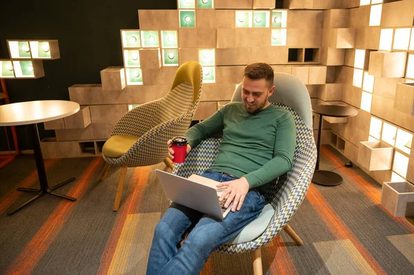 Caucasian Bearded Man Sits Comfortable Chair Drinks Coffee Works Laptop — 图库照片