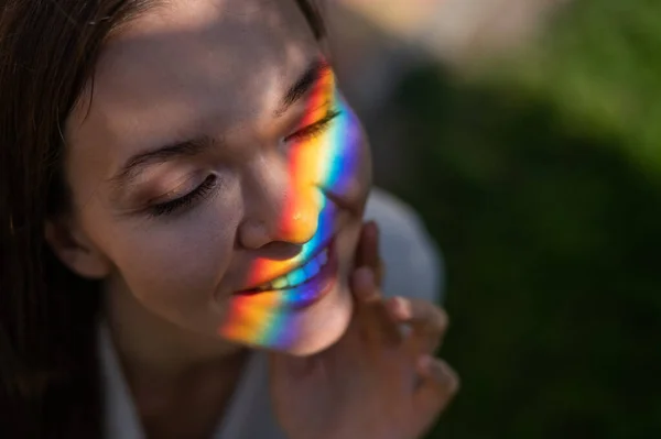 Portrait of caucasian woman with rainbow beam on her face outdoors