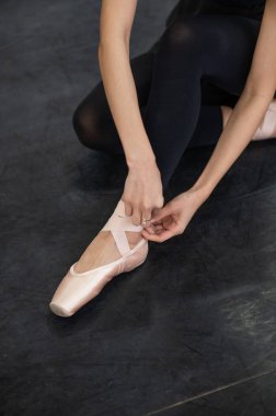 A faceless woman puts on pointe shoes. Close-up of ballerinas legs