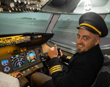 Uçuş simülatörü kullanırken gülümseyen beyaz sakallı bir adam. Pilot kokpitte baş parmak gösteriyor.