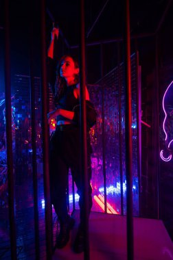 Çelik parmaklıkların arkasındaki neon stüdyodaki beyaz kadın.