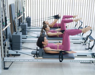 Pembe spor kıyafetli üç Asyalı kadın ıslah yatağıyla pilates egzersizi yapıyor.