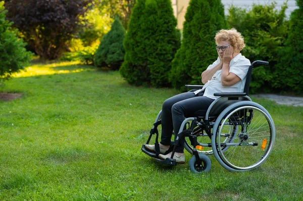 Unhappy elderly woman crying while sitting in a wheelchair on a walk outdoors