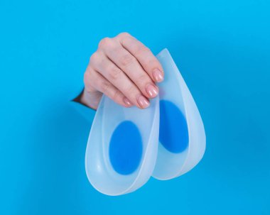 Elinde ortopedik silikon topuklu pedler tutan bir kadın. Bir kadın elleri karton mavi bir arka planda bir delikten sarkıyor.