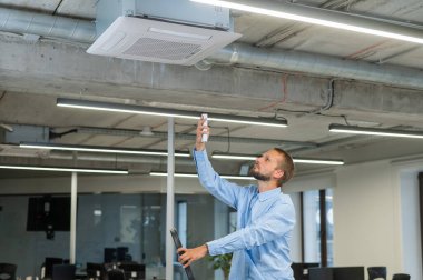 Beyaz sakallı adam ofisteki klimayı tamir ediyor.