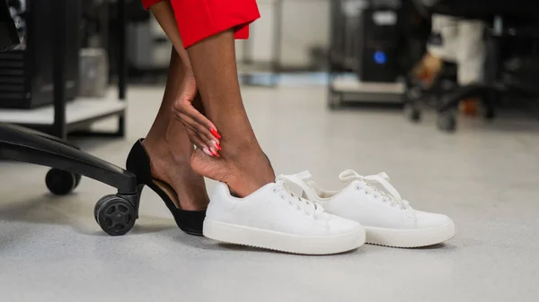 Μια Αφρικάνα Αλλάζει Από Ψηλοτάκουνα Αθλητικά Παπούτσια Στο Γραφείο Κουρασμένα — Φωτογραφία Αρχείου