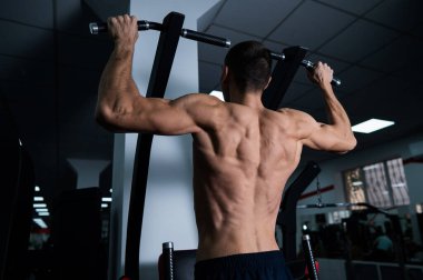 Back view of shirtless man with pull-ups in gym