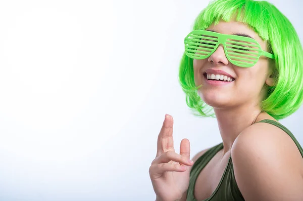 Cheerful young woman in green wig and funny glasses celebrating st patricks day on a white background.