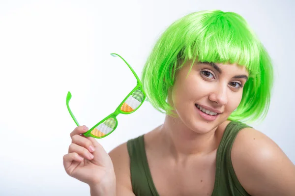 Cheerful young woman in green wig and funny glasses celebrating st patricks day on a white background.
