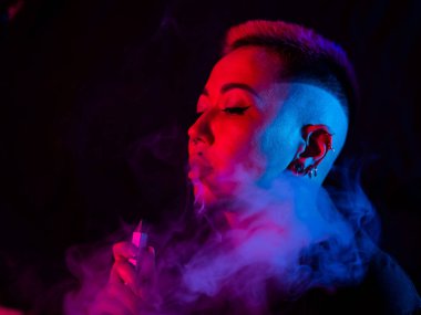 Tıraşlı şakakları olan Asyalı bir kadın neon ışıkta sigara içiyor.