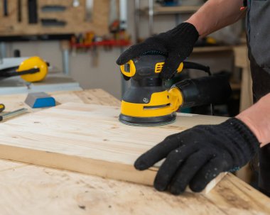 Atölyede çim biçme makinesi kullanan bir adam. Bir marangozun ellerine yakın çekim