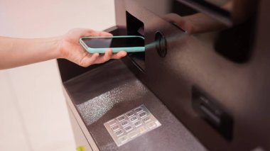 ATM 'de akıllı telefon kullanan bir kadın. NFC çevrimiçi bankacılık kavramı
