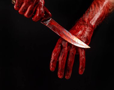 Bir adam kanlı bir bıçağı siyah bir arka planda siliyor.