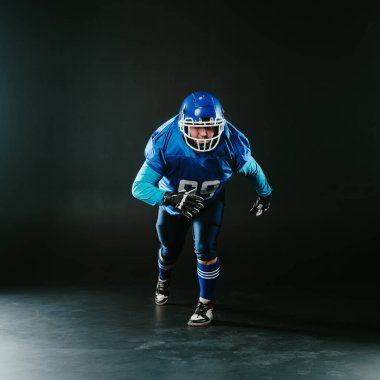 Amerikan futbolu için mavi üniformalı bir adamın portresi siyah arka planda bir topla koşuyor.