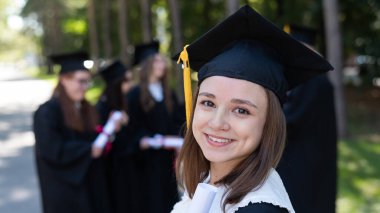 Group of happy students in graduation gowns outdoors. A young girl is happy to receive her diploma