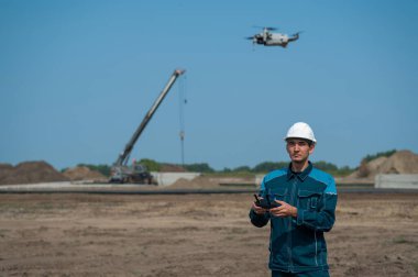 Kasklı ve tulumlu bir adam inşaat alanındaki bir dronu kontrol ediyor. İnşaatçı teknik bir hata yapıyor.