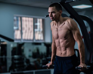 Shirtless man doing triceps dips from parallel bars in gym