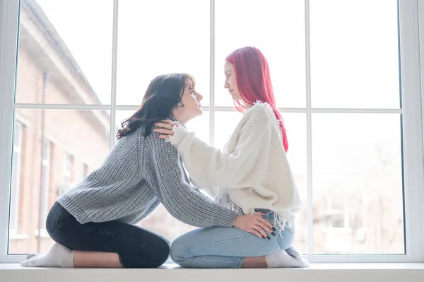 Dwie Kobiety Ubrane Swetry Siedzą Przy Oknie Delikatnie Się Przytulają — Zdjęcie stockowe