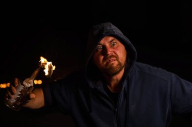 Kapüşonlu adam yanan bir şişe tutuyor. Molotof kokteyli