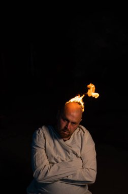 Kel bir adam, deli gömleği ve koyu bir arka planda yanan bir kafası var.