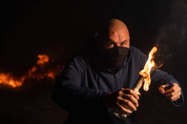 Maskeli bir adam yanan bir şişe tutuyor. Molotof kokteyli