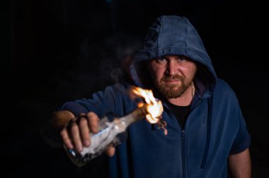 Kapüşonlu adam yanan bir şişe tutuyor. Molotof kokteyli