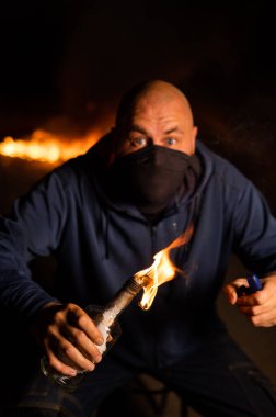 Maskeli bir adam yanan bir şişe tutuyor. Molotof kokteyli