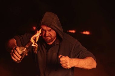 Kapüşonlu adam yanan bir şişe tutuyor. Molotof kokteyli