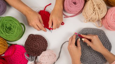 Beyaz bir masada örgü ören kadın elleri. İki kadın pamuk sepetleri örüyor.