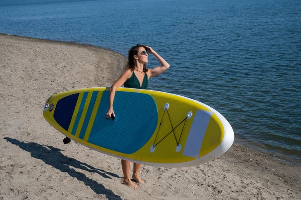 白人妇女沿着海滩散步 并在城市的河边带着一块冲浪板 夏季体育 — 图库照片