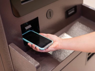 ATM 'de akıllı telefon kullanan bir kadın. NFC çevrimiçi bankacılık kavramı
