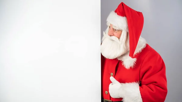 Santa claus peeks out from behind an empty Christmas advertisement and shows a thumbs up