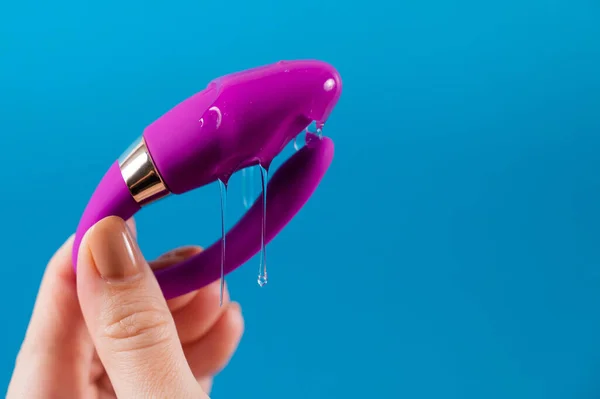 青い背景で潤滑に湾曲したセックスのおもちゃを持っている女性 膣口バイブレータ — ストック写真