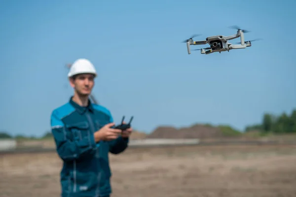 stock image A man in a helmet and overalls controls a drone at a construction site. The builder carries out technical oversight