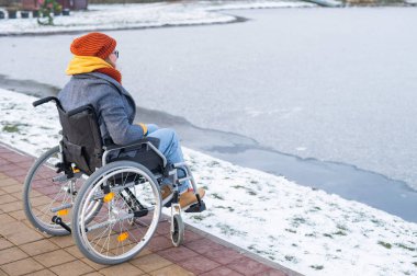 Tekerlekli sandalyedeki beyaz kadın kışın gölün kenarında yürür.