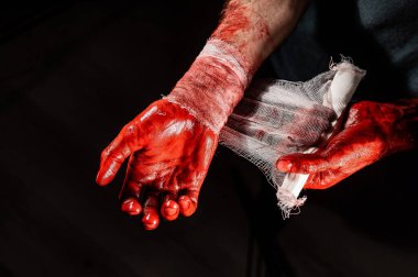 Kanla kaplı bir adam ellerini bandajlıyor.