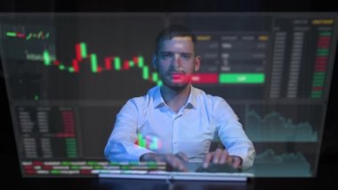 Beyaz adam sanal ekranın önünde karanlıkta oturur ve klavyeye yazı yazar. Stok çizelgeleri