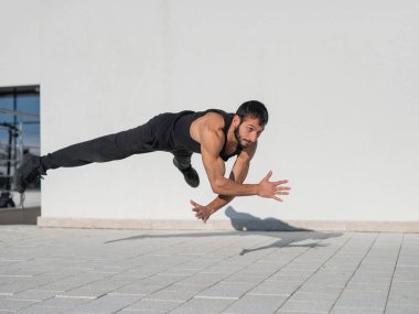 Siyah spor kıyafetli bir adam dışarıda şınav çekerken zıplıyor.