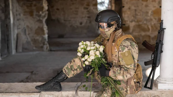 Caucasian woman in military uniform holding a machine gun and a bouquet of white roses